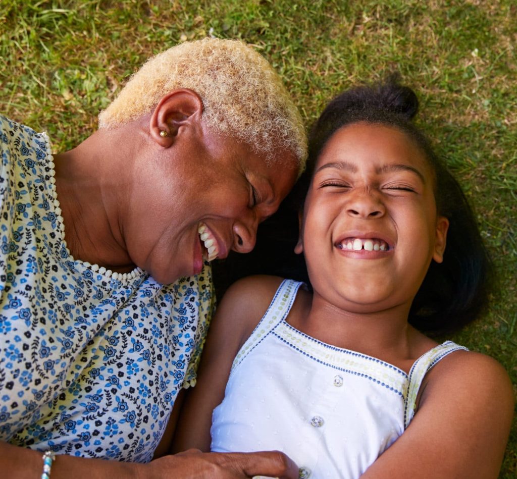 An African American mother with her daughter in the grass laughing
