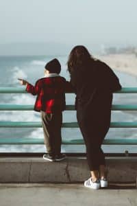Child and parent standing on a bridge leaning on the railing looking at the waves. A walk with your child can help to calm them down from anxiety or a panic attack. 