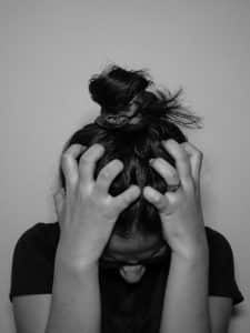A female with her hands in her hair, head bent forward and eyes squeezed shut. Anxiety and panic attacks are difficult and exhausting.